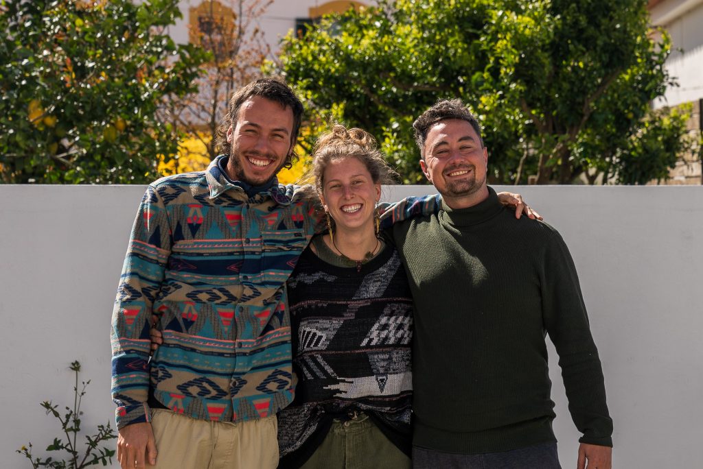 Dynamic and diverse team of Soulwalk Studio gathered in the serene setting of Alentejo, Portugal, showcasing a mix of creative professionals ranging from filmmakers, graphic designers, to project managers, all smiling and radiating positive energy, symbolizing collaboration and shared passion for creativity and sustainable impact.